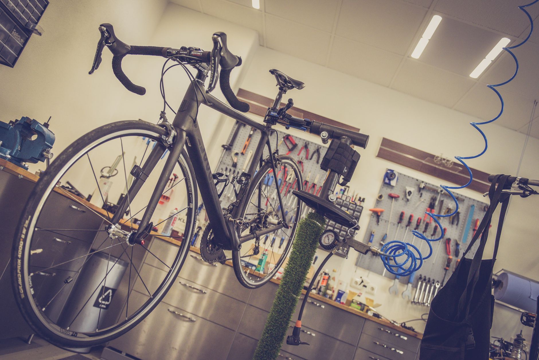 vélo de route noir fixé sur un pied d’atelier dans un magasin, avec des outils accrochés au mur