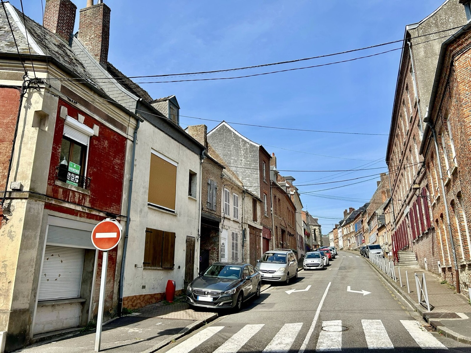 rue en pente de Vervins bordée de maisons de ville en brique et en pierre, voitures garées